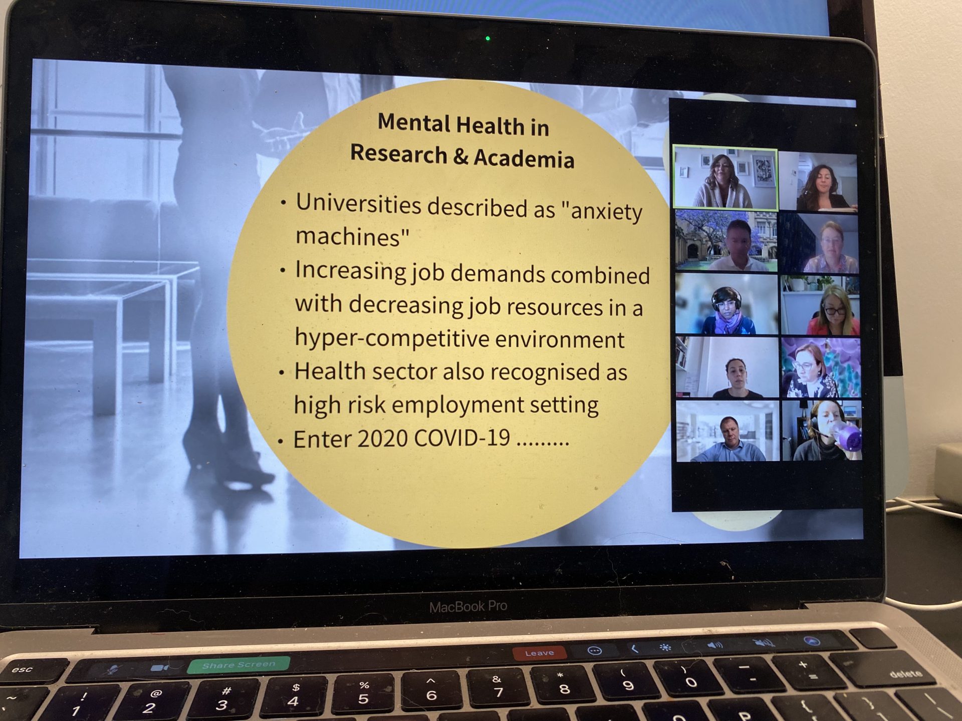 Laptop screen showing a slide from Angela Martin. The heading is Mental Health in Research and Academia. The dot points read: Universities described as "anxiety machines"; Increasing job demands combined with decreasing job resources in a hyper-competitive environment; health sector also recognised as high risk employment setting; Enter 2020 COVID-19