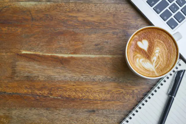 Desk with coffee, laptop, notebook & pen