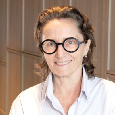 A professional photograph of a woman in a white shirt wearing glasses and smiling at the camera