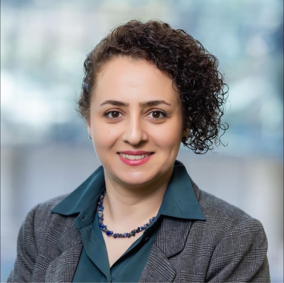 Dr Afsaneh Lahooti A professional headshot of a woman wearing a suit against a blurred blue background